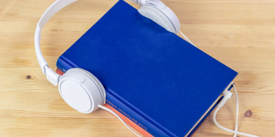 Libro con auricular colocado sobre él, simulando que el libro está escuchando un audio.