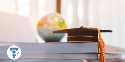 Un gorro de graduación y un globo terráqueo apoyados sobre un libro de estudio.